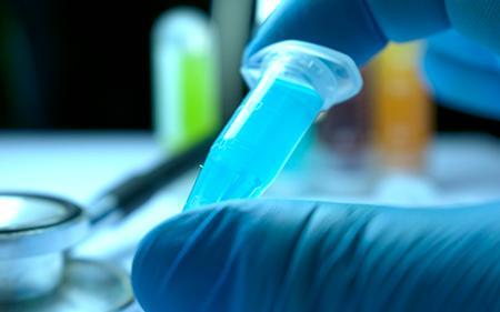 A laboratory technician holding a tube containing liquid for use in medical research.